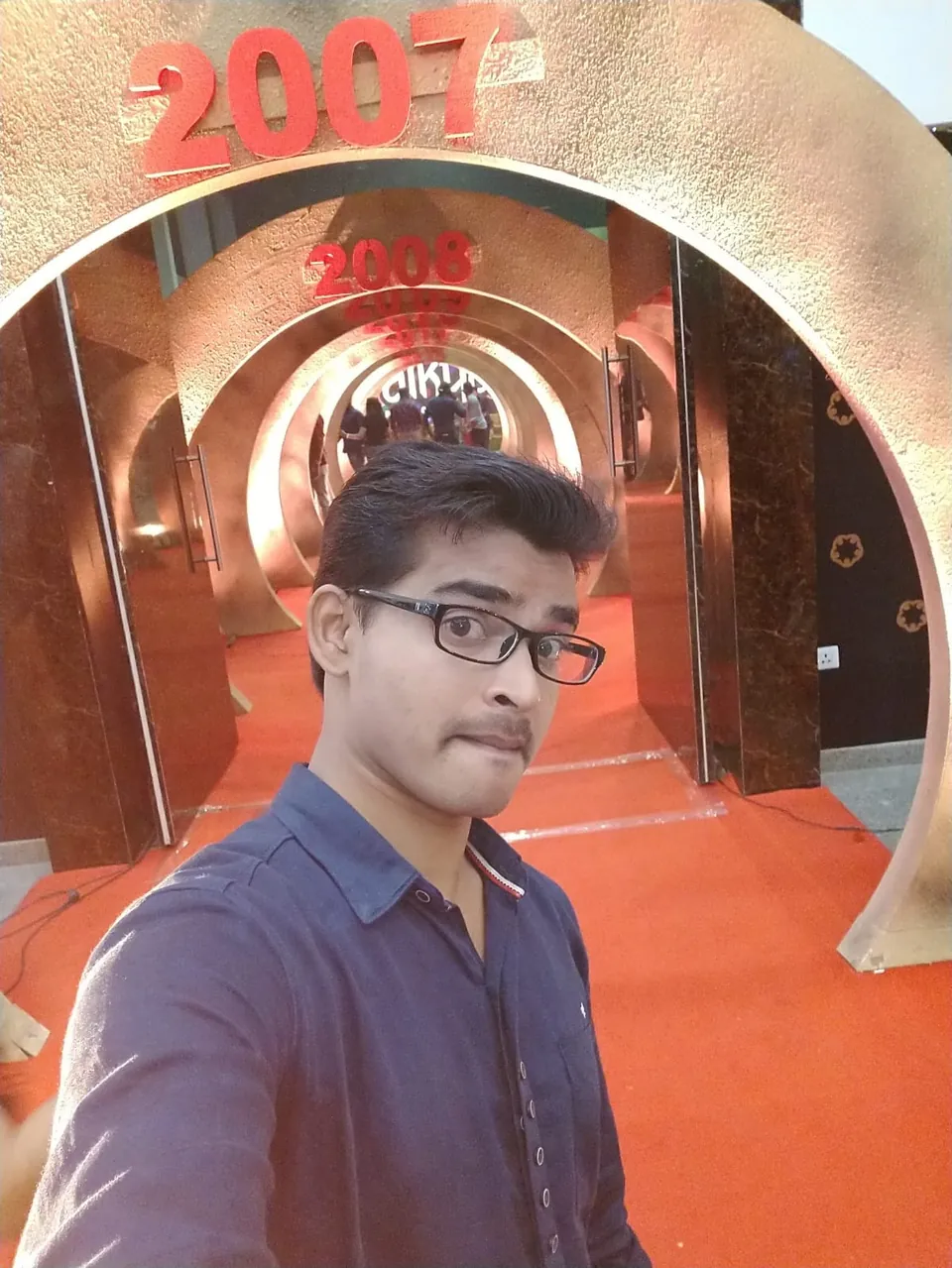 Selfie of Krishna Kummari in front of a decorated tunnel of arches marked with years, the nearest reading 2007.