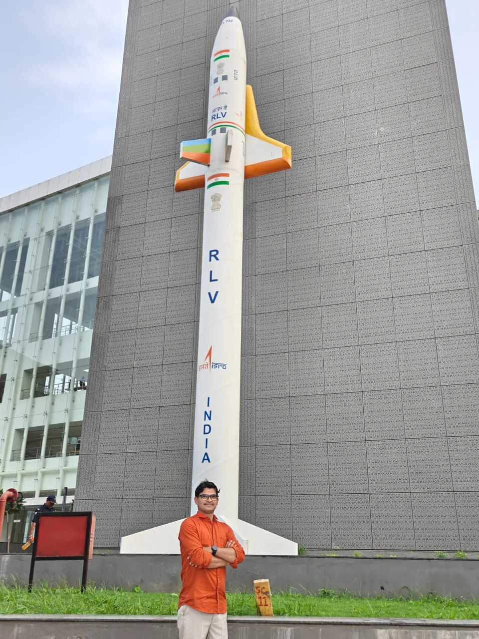 Krishna Kummari standing below a tall white model of a winged vehicle marked RLV and India, mounted on a grey tower.