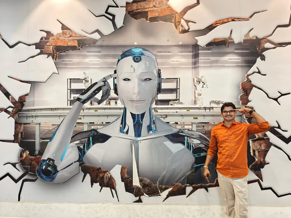 Krishna Kummari saluting playfully beside a large painted mural of a robot breaking through a wall.